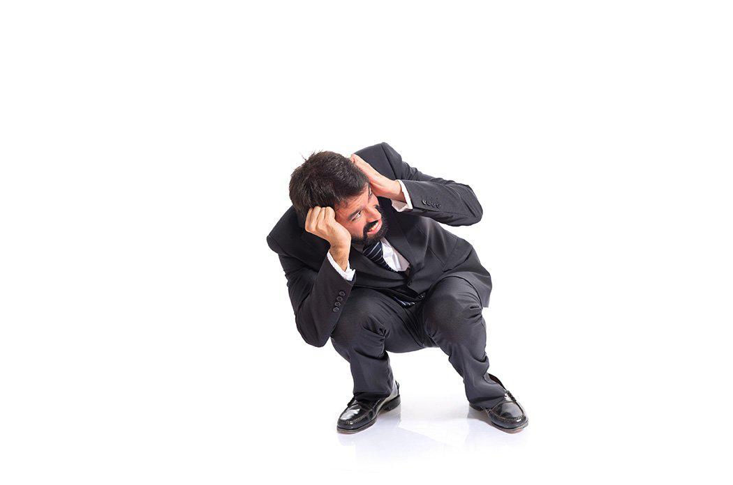 Man in suit squatting down while covering ears