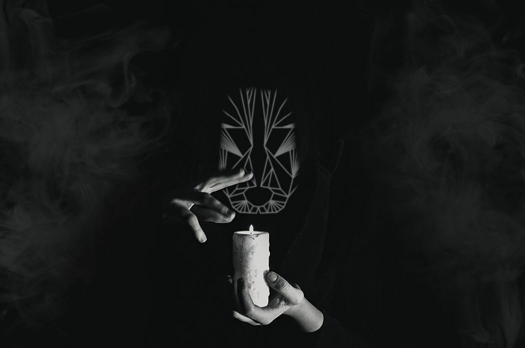 Black and white cloaked masked person holding a white candle