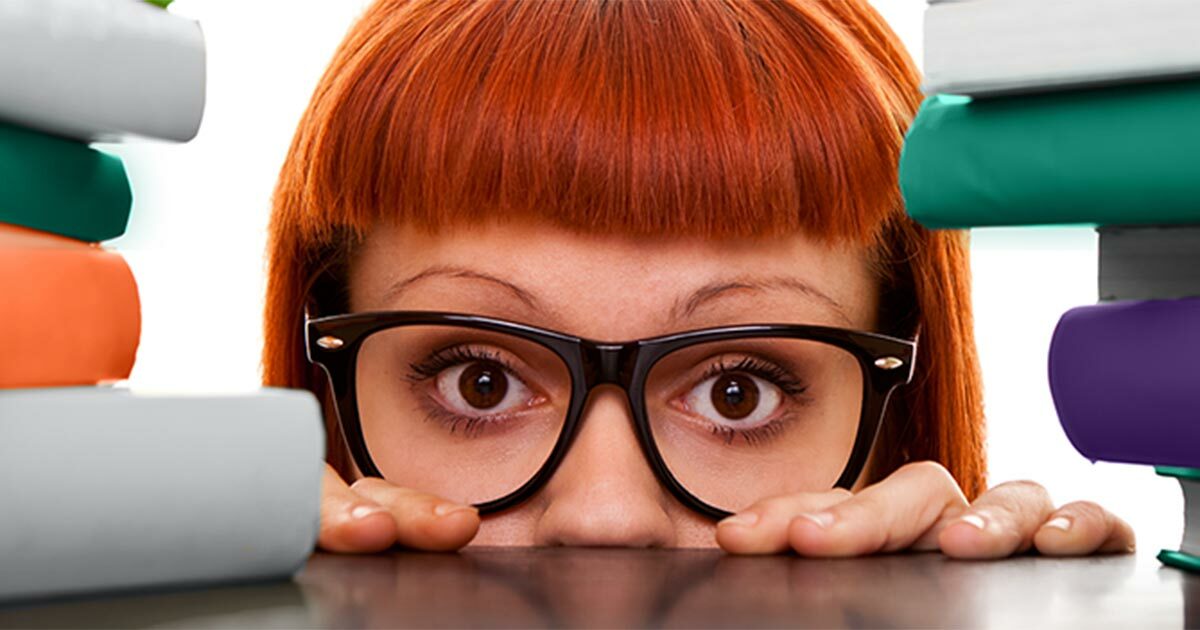 Red headed women with glasses peering over a counter between cybersecurity books