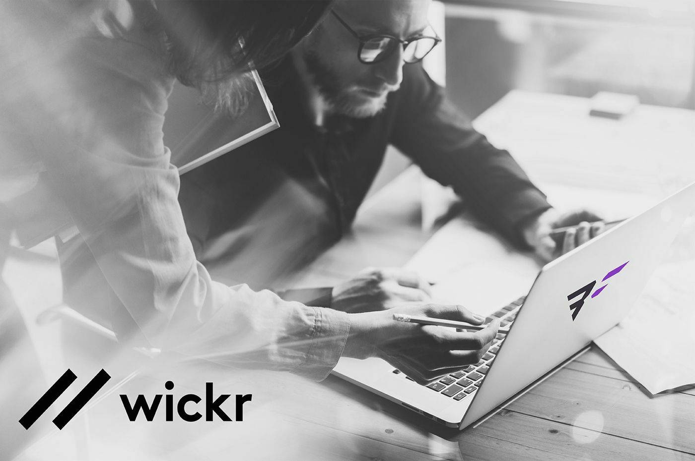 Person working on laptop other person leaning over with pencil in hand