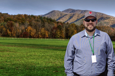 Man with hat on standing in front of trees and mountains