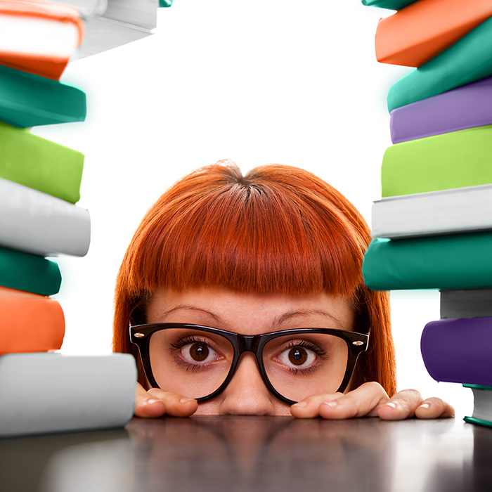 Red headed women with glasses peering over a counter between books